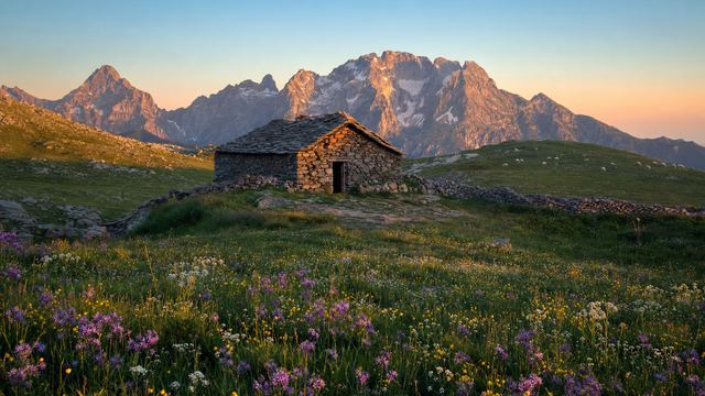 Estive pyrénéenne avec cabane de pierre, troupeau de brebis et crêtes rocheuses en arrière-plan sous un ciel clair